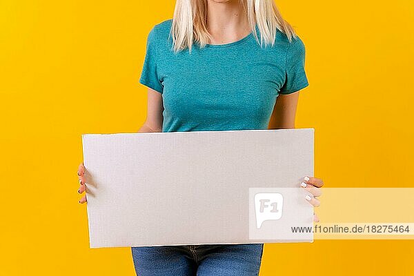 Weißes leeres Werbeplakat in der Hand  blondes kaukasisches Mädchen auf gelbem Studiohintergrund