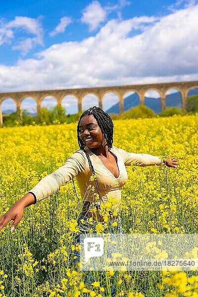 Lifestyle  lächelnd die Natur genießen  Porträt eines schwarzen ethnischen Mädchens mit Zöpfen  Reisende  in einem Feld mit gelben Blumen