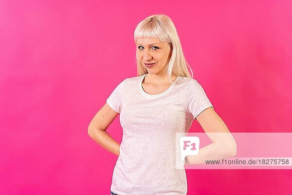Lächelndes  verstecktes Geschenk für die Kamera  blondes  kaukasisches Mädchen im Studio auf rosa Hintergrund