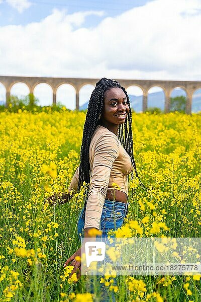 Lebensstil  Genießen der Natur  Porträt eines schwarzen ethnischen Mädchens mit Zöpfen  Reisende  in einem Feld mit gelben Blumen