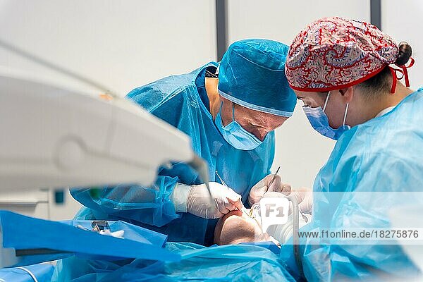 Zahnklinik  Zahnärztinnen in blauen Anzügen und Hüten führen eine orale Operation durch