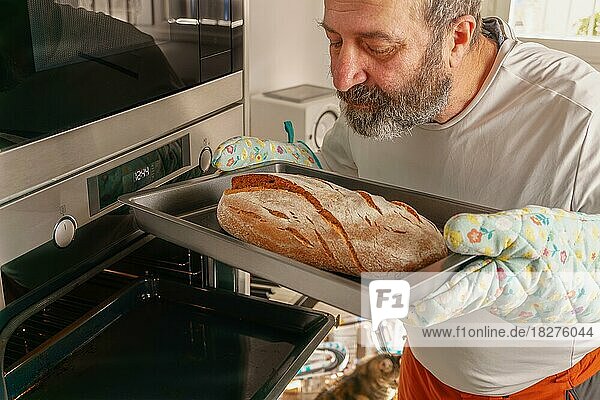 Älterer Mann mit Bart schiebt Brot in den Ofen seines Hauses