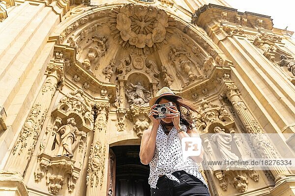 Eine Frau mit Hut  die die Stadt besichtigt und mit einer alten Kamera Fotos macht und den Sommerurlaub genießt  Konzept einer weiblichen Reisenden oder Urlauberin und Erstellerin digitaler Inhalte