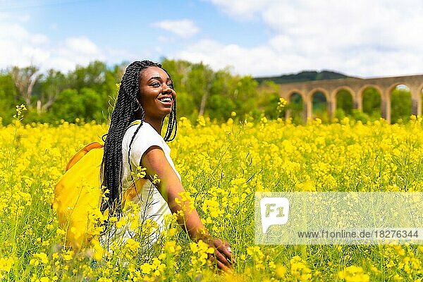 Ein schwarzes ethnisches Mädchen mit Zöpfen  eine Reisende  genießt die Freiheit in einem gelben Blumenfeld
