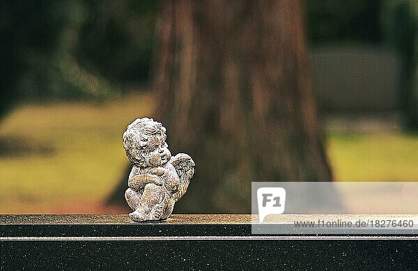 Kleine Engelsfigur sitzt auf einem Grabstein  Baum im Hintergrund  Deutschland  Europa