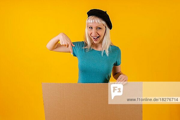 Zeigen lächelnd Karton Werbeplakat  blonde kaukasische Mädchen auf gelben Studio Hintergrund