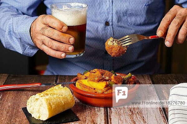 Mann mit Bart und blauem Hemd isst Fleischbällchen mit Spaghetti in einem Restaurant mit einem Glas Bier in der Hand