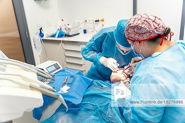 Zahnklinik  Zahnärzte in blauen Anzügen führen eine Operation an einem Implantat durch
