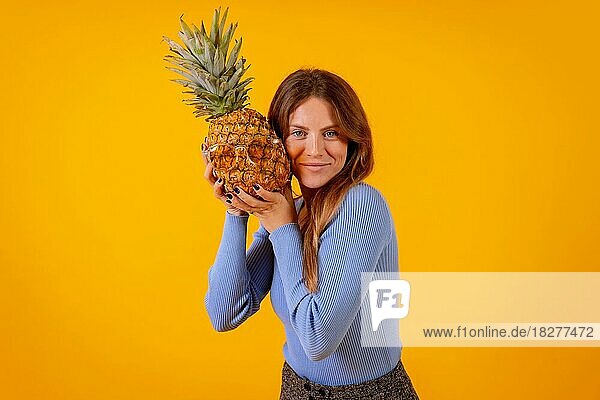 Frau lächelnd mit einer Ananas in Sonnenbrille in einem Studio auf einem gelben Hintergrund  gesund  Sommer