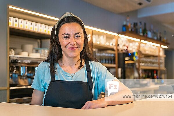 Porträt einer hübschen  lächelnden Kellnerin mit der Kaffeemaschine im Hintergrund  die Beschränkungen für den Aufenthalt im Freien und die obligatorische Verwendung von Masken werden aufgehoben