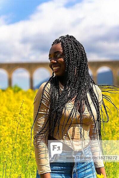 Lifestyle mit bewegtem Haar  Porträt eines schwarzen ethnischen Mädchens mit Zöpfen  Reisende  in einem Feld mit gelben Blumen
