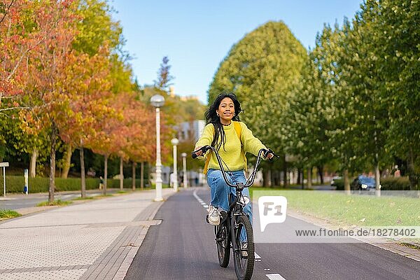 Junge asiatische Studentin auf dem Fahrrad auf dem Weg zur Universität entlang des Radwegs  gesundes Leben  umweltfreundlich