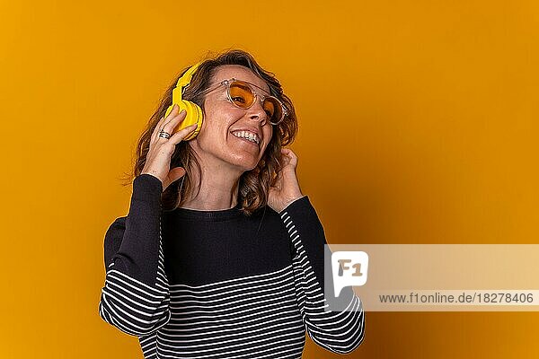 Caucasian girl listening to music smiling on her phone with headphones and sunglasses  yellow background