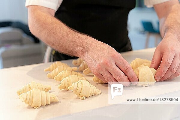 Hände eines Mannes  der zu Hause kleine Croissants bäckt und sie fertig bearbeitet