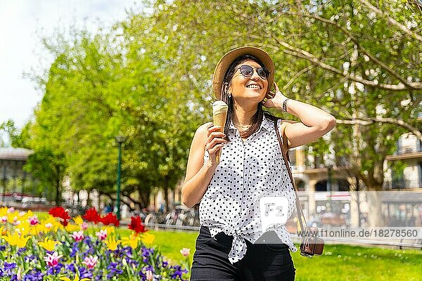 A tourist woman visiting the city eating an ice cream cone  enjoying summer vacations and with a camera  solo female traveler concept  wearing sunglasses