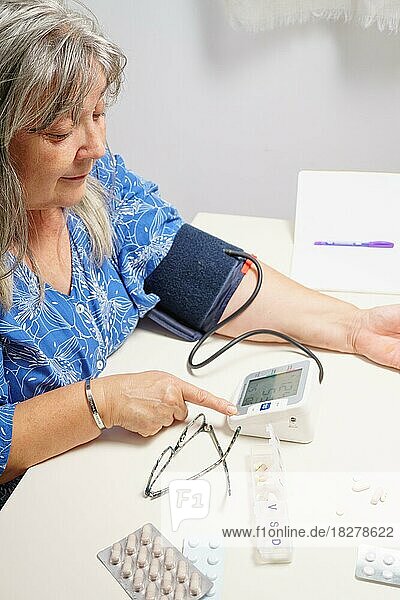Older white-haired woman with glasses taking her blood pressure at home with white background