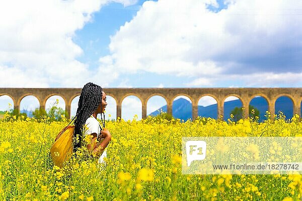 Genießen Sie den Frühling  schwarzes ethnisches Mädchen mit Zöpfen  Reisende  in einem Feld von gelben Blumen