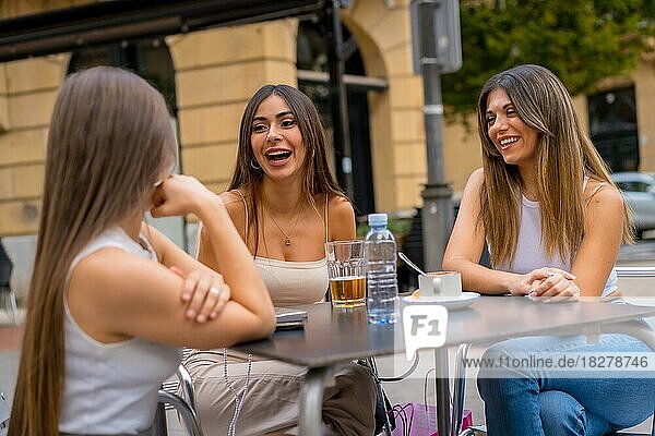 Portrait of young women friends having something one afternoon on a terrace of a cafeteria in autumn