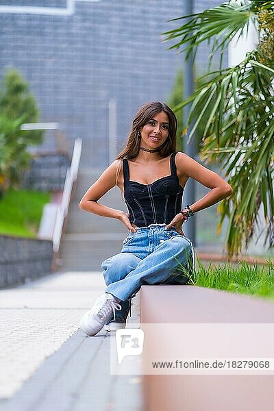 Porträt eines jungen brünetten Models mit schwarzer Kappe und Jeans in der Stadt sitzend