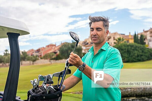 Mann spielt Golf in einem Golfclub und überprüft die Golfschläger im Buggy  bevor er zu spielen beginnt
