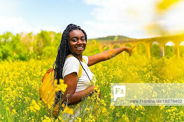 Zeigt auf ein schönes Aquädukt  ein schwarzes ethnisches Mädchen mit Zöpfen  eine Reisende  in einem Feld mit gelben Blumen
