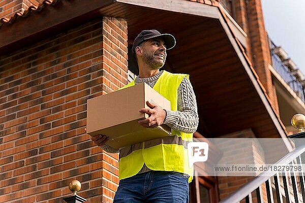 Paketzusteller eines Online-Shops  mit einer Schachtel in der Hand auf der Treppe des Hauses