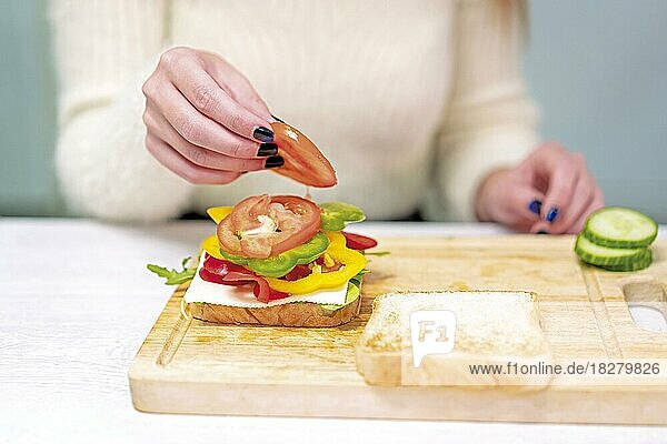 Unbekannte Person  die zu Hause in der Küche ein Gemüsesandwich zubereitet. Sie bereitet es vor  indem sie die Tomate