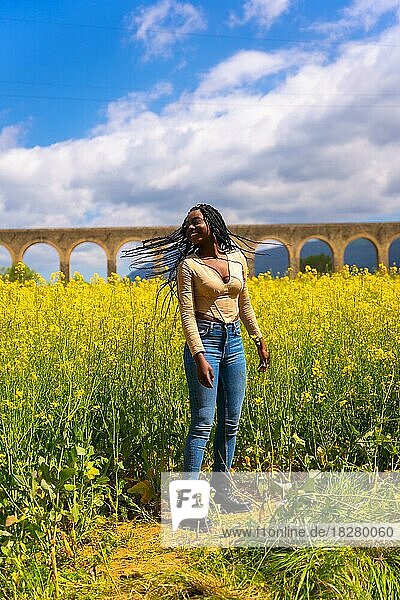 Lächelnder Lebensstil in der Natur  ein Mädchen schwarzer Herkunft mit Zöpfen  eine Reisende  in einem Feld mit gelben Blumen