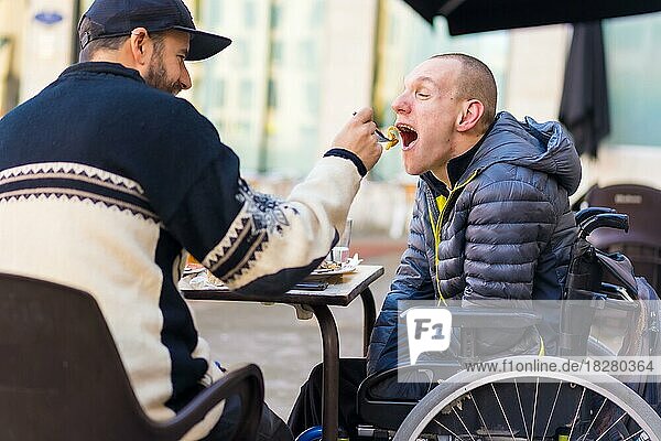 A disabled person eating with the help of a friend having fun  terrace of a restaurant
