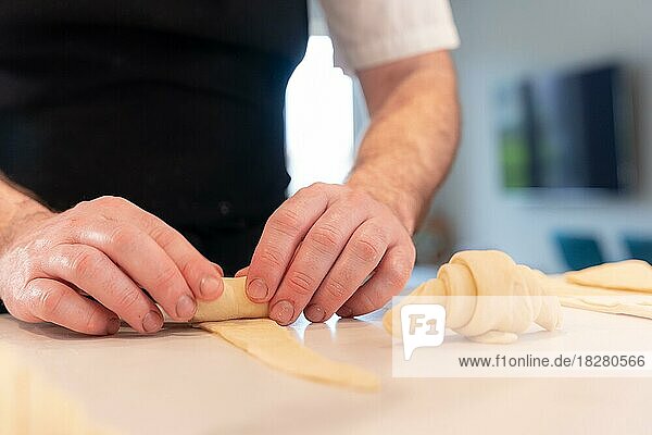 Hände eines Mannes  der zu Hause kleine Croissants backt  die mit dem Blätterteig geformt werden