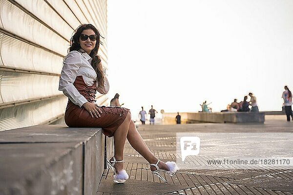 Portrait of a pretty brunette woman in a leather skirt sitting in a sunset wearing sunglasses