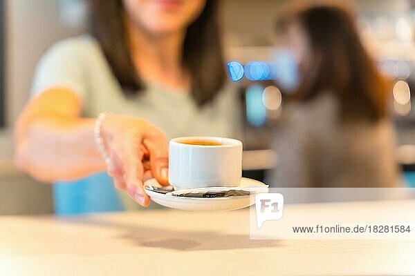 Hände einer Kaffeehausbesitzerin mit einem Milchkaffee in der Hand  die dem Kunden den Kaffee anbietet