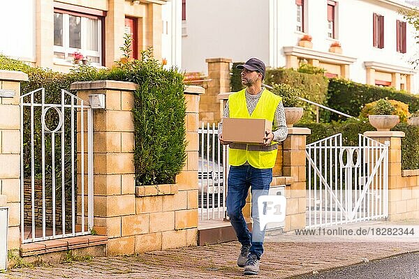 Paketzusteller eines Online-Shops  der mit einem Karton in der Hand das Haus sucht