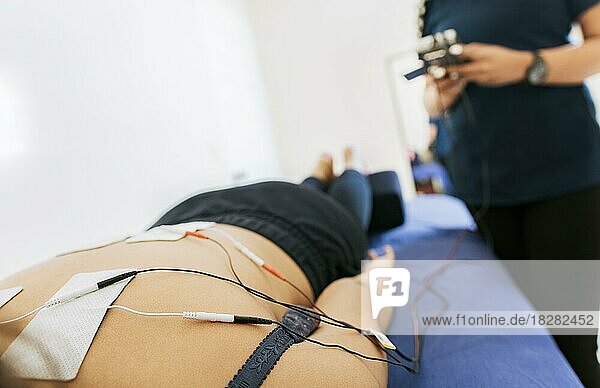 Elektrodenbehandlung am liegenden Patienten  Professioneller Physiotherapeut elektrostimuliert einen liegenden Patienten. Physiotherapeutin bei Elektrostimulation eines Patienten  Therapie des unteren Rückens mit Elektrodenpads