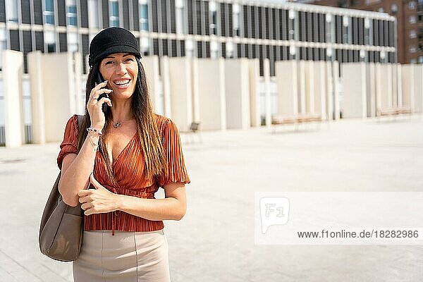 Eine Geschäftsfrau vor dem Büro  die einen Anruf tätigt  mit braunem Hemd und schwarzem Hut