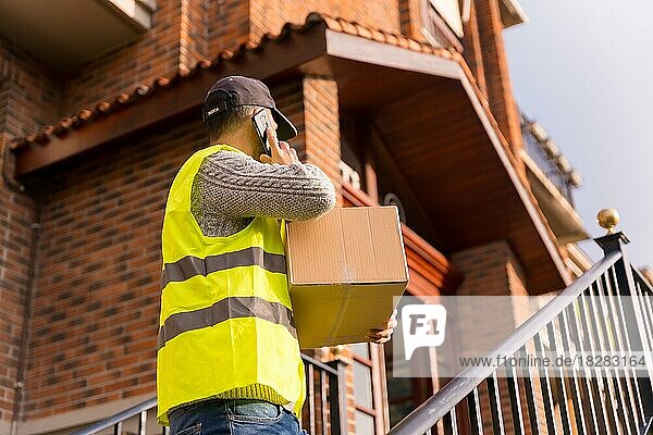 Paketzusteller eines Online-Shops  mit einer Schachtel in der Hand auf der Treppe des Hauses