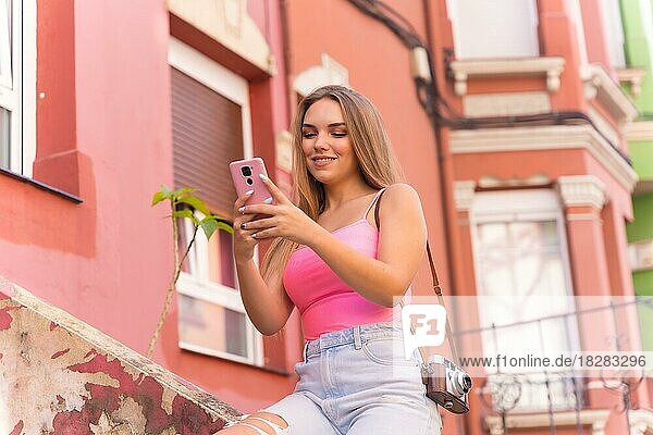 Junge blonde kaukasische Touristin in einer Straße mit Häusern mit bunten Fassaden  Blick auf das Telefon