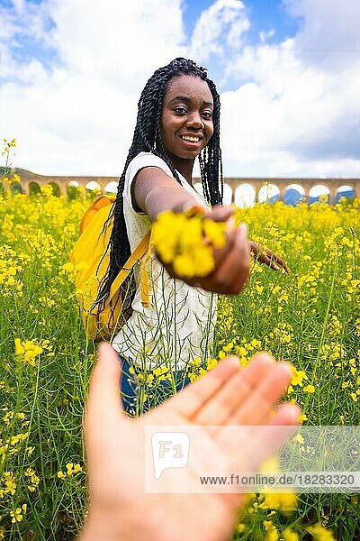 Ein schwarzes ethnisches Mädchen mit Zöpfen  eine Reisende  bietet eine Blume in einem gelben Blumenfeld an