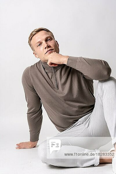 Caucasian blond model with a brown sweater on a white background  sitting on the floor with a seductive look