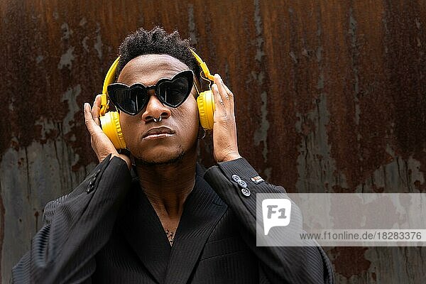 Schwarzer ethnischer Mann  der Musik hört  drahtlose gelbe Kopfhörer  mit Herz-Sonnenbrille  hört moderne Musik