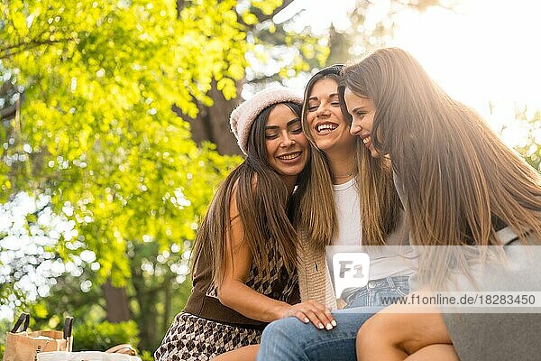 Women friends sitting hugging in a park in autumn at sunset  lifestyle and autumnal outfit