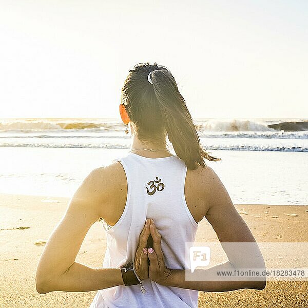 Rückansicht einer jungen Frau  die am Strand Yoga übt