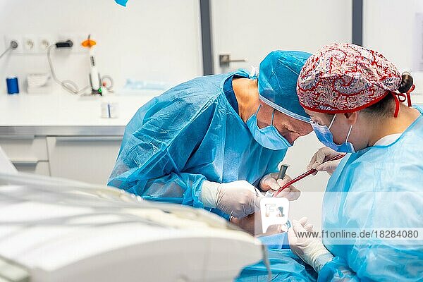 Zahnklinik  Zahnarzt und die Assistentin in blauen OP-Anzügen bei der Arbeit mit einer Kundin