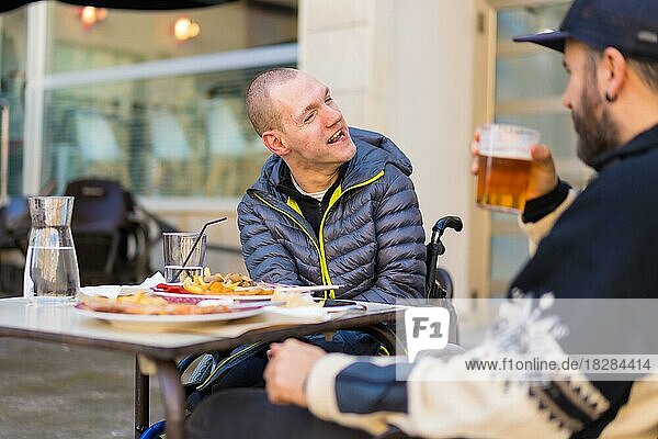 A disabled person eating and smiling with a friend having fun  terrace of a restaurant