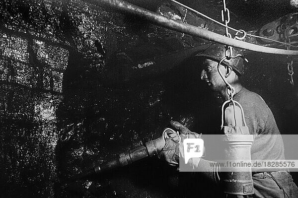 Bergmann  Hauer  der unter Tage in einem Schacht arbeitet und Kohle von Hand mit einem Presslufthammer und einer Hacke in einem Bergwerk fördert