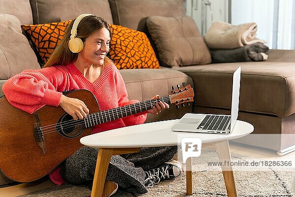 Frau lernt Gitarre spielen zu Hause mit Online-Unterricht am Computer  nach den Noten