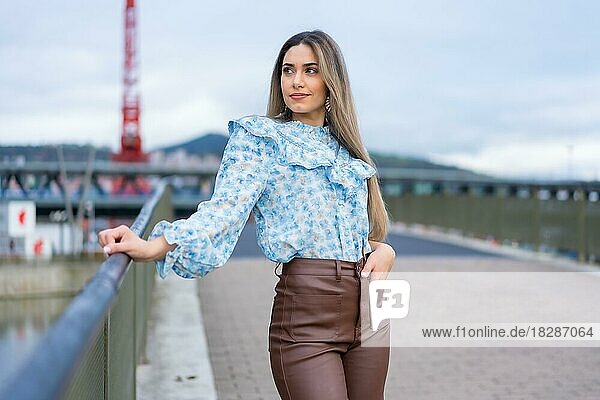 Portrait young woman on a city river bridge  lifestyle concept  blue shirt and brown pants