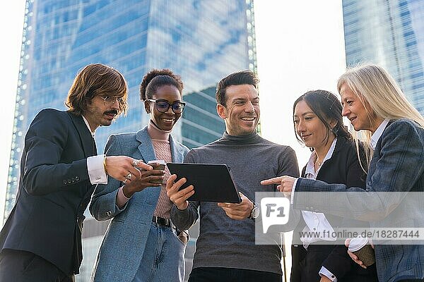 Eine Gruppe multiethnischer Geschäftsleute in einem Gewerbegebiet schaut lächelnd auf ein Tablet