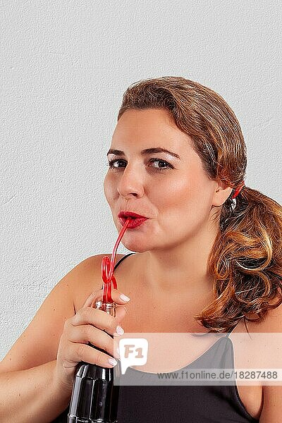 Porträt einer molligen Frau  die mit einem Strohhalm aus einer Flasche trinkt