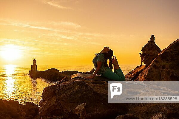 Anjaneyasana  Eine Frau macht Meditations- und Yogaübungen bei Sonnenuntergang neben einem Leuchtturm im Meer  gesundes und naturistisches Leben  Pilates im Freien